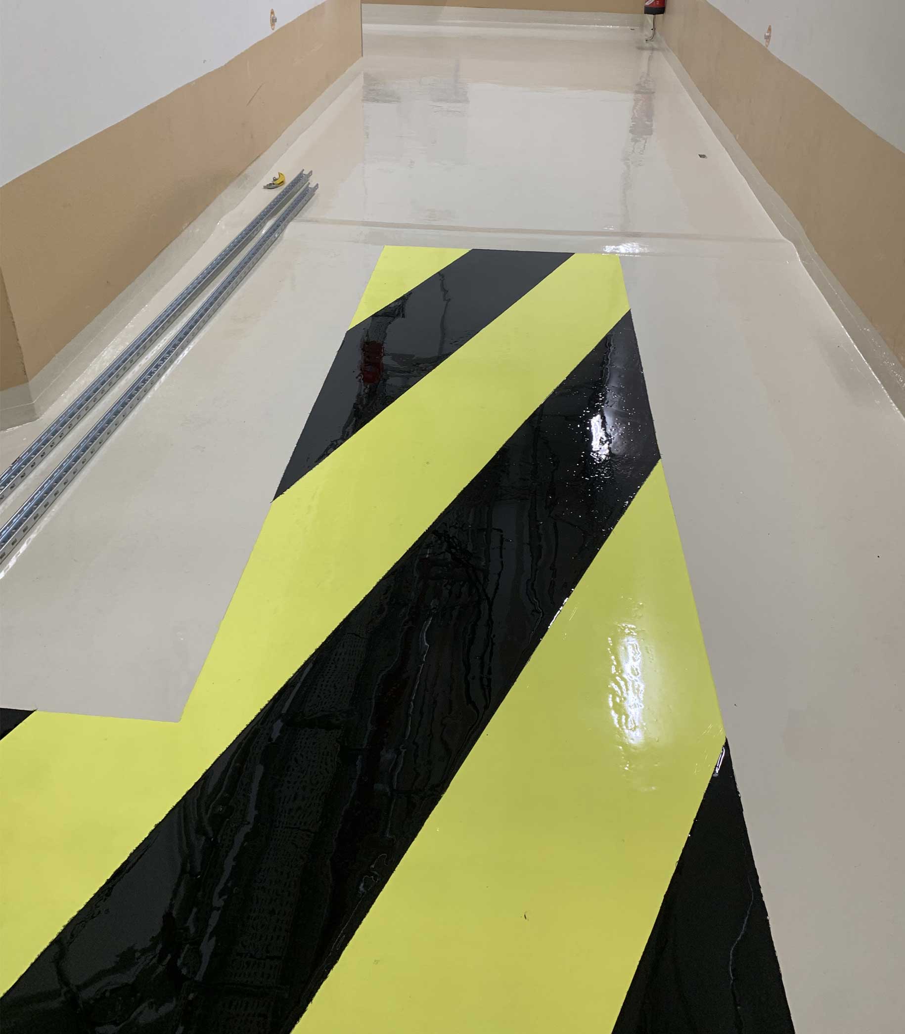 Sol intérieur avec traçage jaune et noir, offrant une signalétique claire et durable, par Kemica Coatings pour des environnements professionnels.